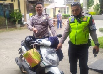 Anggota Polres Kediri menunjukkan motor dan tas yang dibuang pelaku ke sungai. (Foto: bacaini)
