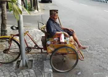 Mbah Wakid duduk di atas becak di kawasan Pagora Kediri. Foto: Bacaini