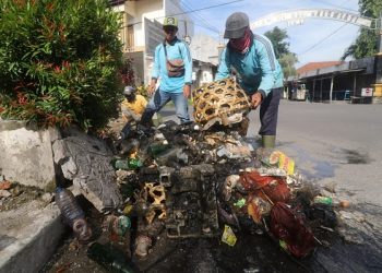 Petugas mengangkat sampah dari saluran drainase yang terhambat kabel fiber optik. Foto: Humas