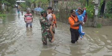 Anggota TNI dan BPBD Jombang gendong anak sekolah melewati jalan tergenang banjir. Foto: Bacaini/Syailendra