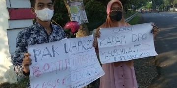 Sepasang aktivis membawa poster tuntutan yang ditujukan kepada Wapres RI saat berkunjung ke Jombang. Foto: Bacaini/Syailendra