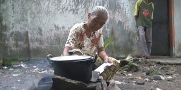 Nur Hayati, istri Khoirul tengah memasak di tungku dengan bahan bakar kayu. Foto: Bacaini/Syailendra