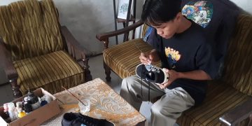 Zayinul Muhajibin sedang melukis sepatu pesanan pelanggan. Foto: Bacaini/Aby