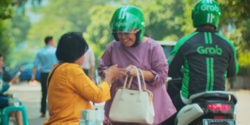 Driver ojek online melintas dengan atribut Grab dan Gojek setelah aturan baru Perpres Ojol 2026 tentang pemotongan komisi aplikasi maksimal 8 persen