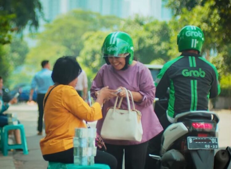 Driver ojek online melintas dengan atribut Grab dan Gojek setelah aturan baru Perpres Ojol 2026 tentang pemotongan komisi aplikasi maksimal 8 persen